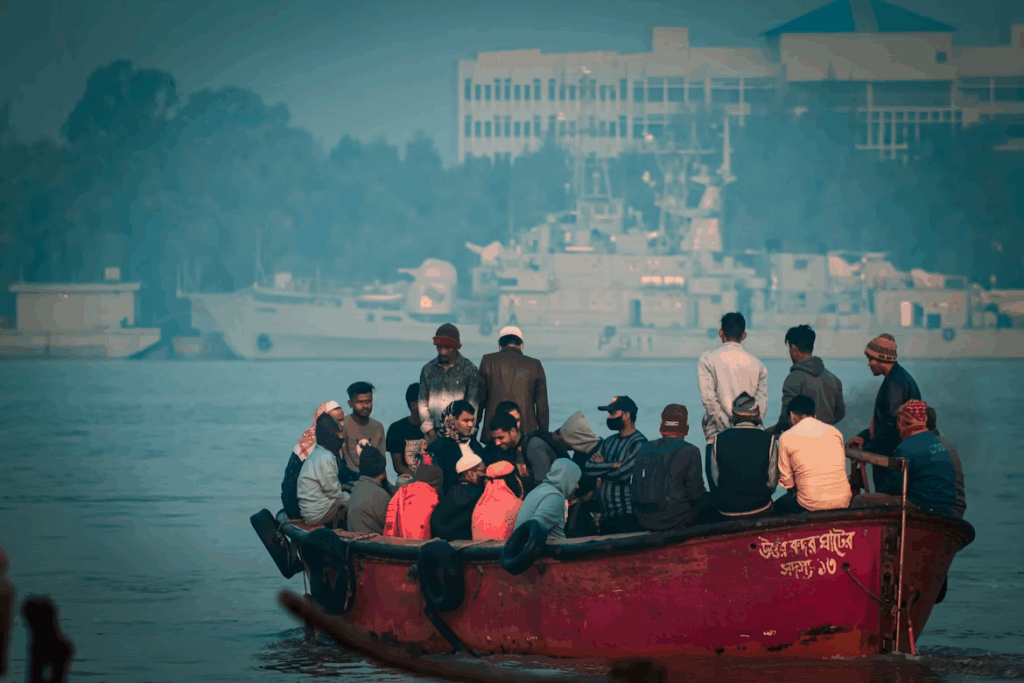 Group of people crowded on a small boat crossing a hazy harbor, symbolizing global climate migration and displacement.