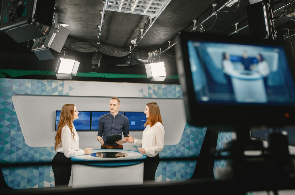 News presenters discussing a segment in a modern television studio, filmed in an AI-driven newsroom.