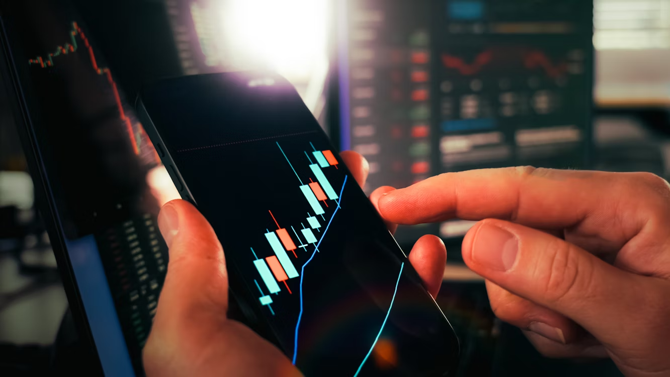 Investor analyzing global stock market trends 2025 on smartphone with candlestick chart.
