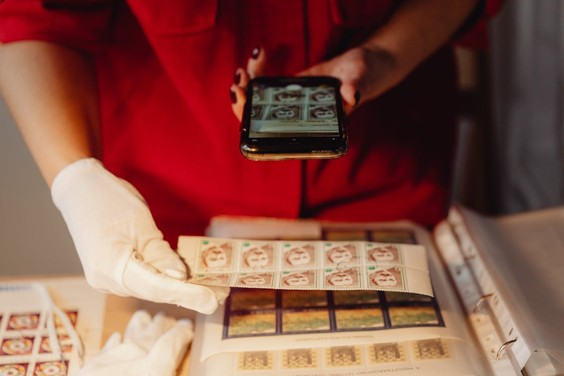 Archivist uses a smartphone to digitize vintage postage stamps for digital cultural preservation.