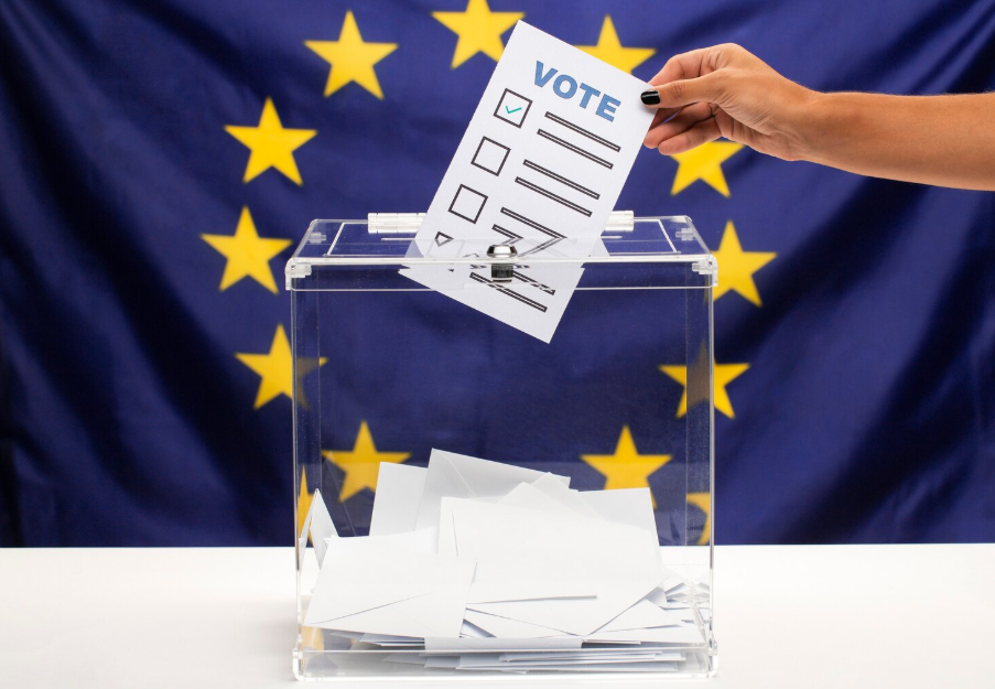 Placing a vote into a clear ballot box in front of an EU flag, symbolizing pivotal global elections in 2025–26.